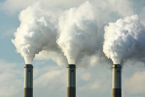 Three smokestack spewing dirty smoke, silhouetted against the sky.